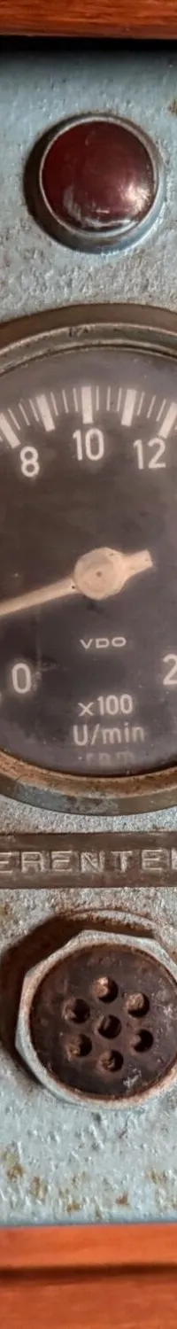 Een lichtblauwe, roestige motorpaneel met drie meters, een rode knop en twee sleutelgaten.