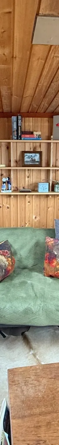 Een houten interieur met een bank, salontafel, planken, ramen en een kachel.