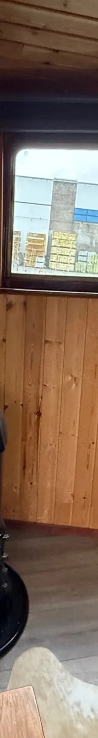Een interieur van een boot met houten wanden, twee ramen, een kachel, een radiator en een bank.