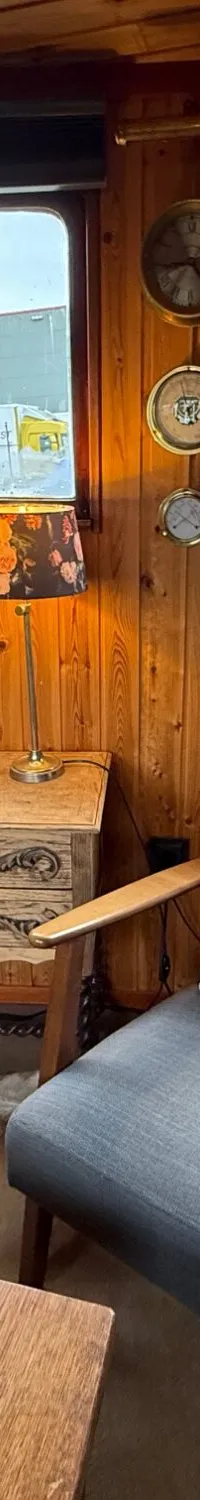 Een interieur van een boot met houten wanden, twee ramen, een bank, een fauteuil en een bijzettafel.
