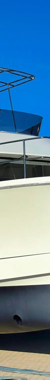 Een witte catamaran met een zwarte romp staat op de wal voor een geel gebouw onder een helderblauwe lucht.