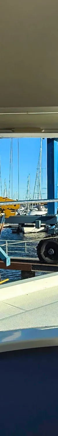Een uitzicht vanaf een boot op een jachthaven met andere boten en een blauwe bootlift onder een heldere hemel.