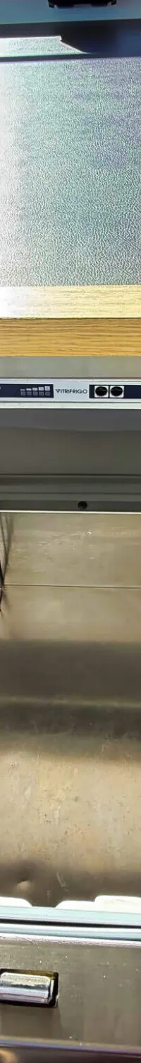 Een open roestvrijstalen koellade met het merk Vitrifrigo, ingebouwd in een houten meubel naast een grijze bank.