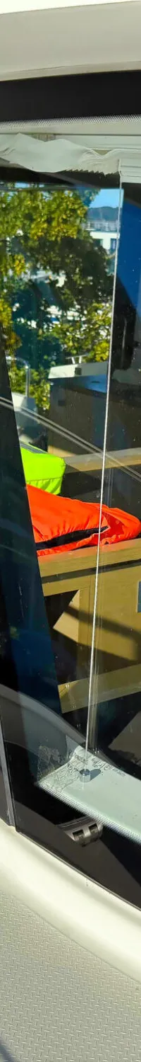 Een witte boot met ramen, met daardoorheen een interieur met oranje en groene reddingsvesten en een uitzicht op water.