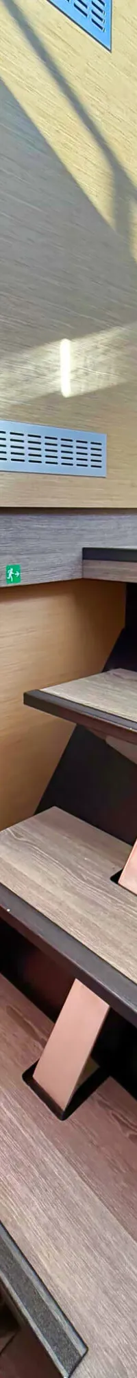 Een houten trap met metalen accenten leidt naar een hoger dek, met een open deur naar een slaapkamer aan de linkerkant.