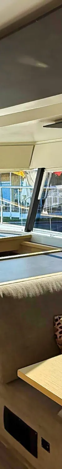 De foto toont het interieur van een boot met een stuurstand, een zithoek met tafel en een keukenblok.