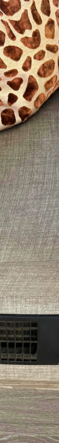 Een grijze stoffen bank met een kussen met bruine vlekken, een houten tafel en een ventilatierooster met schakelaar.