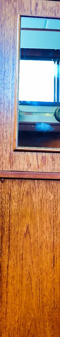 Een houten interieur van een boot met een decoratief scheepsroer aan de muur, een spiegel en een trap.