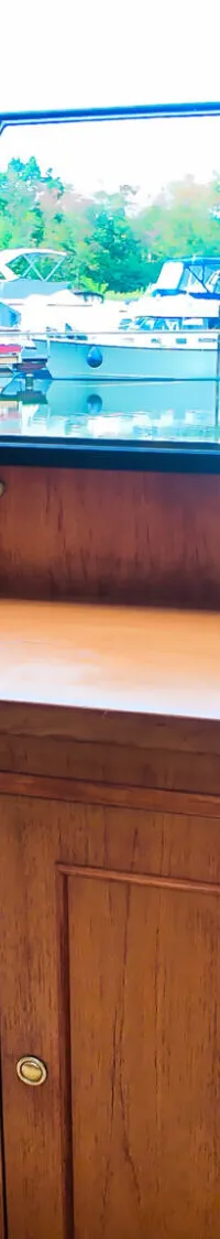 Een interieur van een boot met houten kasten, een televisie, een lamp, een modelboot en een raam met uitzicht op andere…