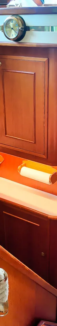 Een interieur van een boot met een kombuis, houten kasten, een oven, een spoelbak en een trap met touwleuning.