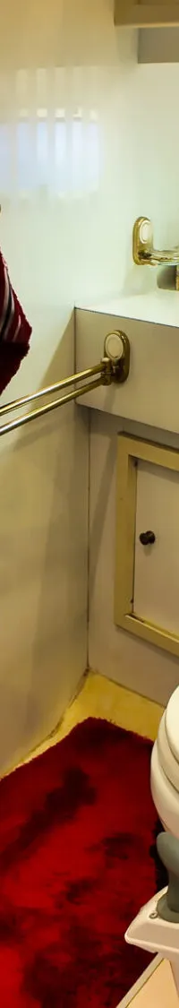 Een badkamer aan boord met een toilet, wastafel, spiegel, douche en een patrijspoort.