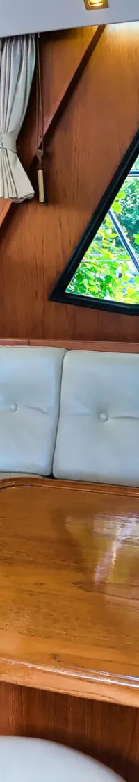 Een interieur van een boot met een houten tafel, een crèmekleurige bank en een stuurstand met een stuurwiel.