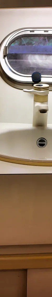 Een witte wastafel met kraan, spiegel, patrijspoort en diverse accessoires in een bootinterieur.