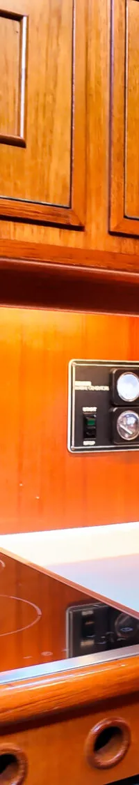 Een houten scheepskeuken met een kookplaat, koffiezetapparaat, magnetron en een patrijspoort.
