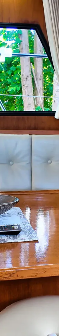 Een houten tafel met een zilverkleurige schaal en twee afstandsbedieningen, omringd door een crèmekleurige bank en krukjes.