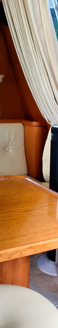 Een interieur van een boot met een houten tafel, een bank met witte kussens en ramen met uitzicht op groen.