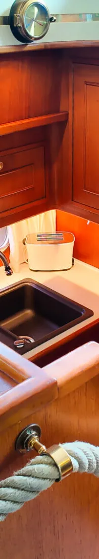 Een houten interieur van een boot met een kombuis, een trap met touwreling en diverse nautische decoraties.