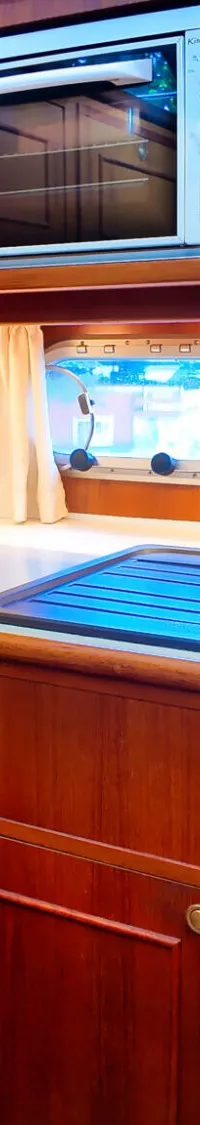 Een houten scheepskeuken met een gootsteen, kookplaat, magnetron, koffiezetapparaat en broodrooster.