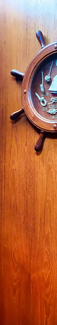 Een interieur van een boot met houten wanden, een decoratief stuurwiel en een spiegel.