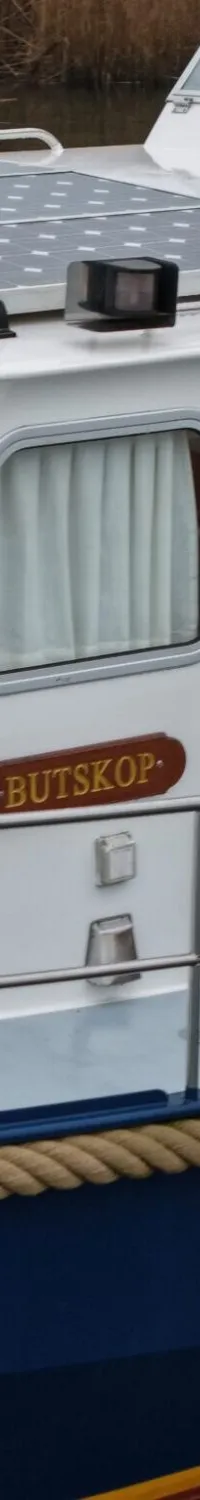 Een witte boot met een blauwe romp, zonnepanelen op het dak en de naam "BUTSKOP" op de zijkant.