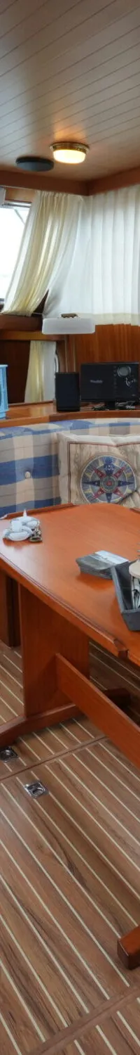 De foto toont het interieur van een boot met houten lambrisering, een geruit bankstel en een houten tafel.