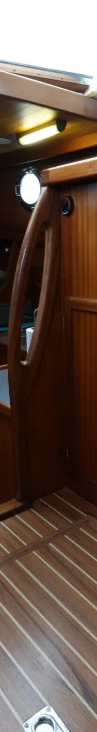 De foto toont het interieur van een boot met houten vloeren, wanden en plafonds, blauw-wit geruite kussens en een rode…