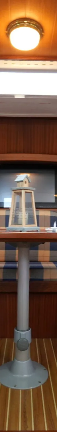 Een houten interieur van een boot met een U-vormige bank met geruite kussens rond een tafel, en een wasmachine.