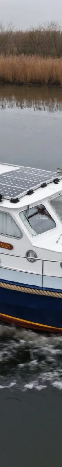 Een blauw-witte motorboot met een donkerblauwe kap vaart over een rivier met rietkragen op de achtergrond.