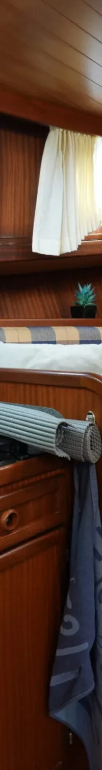 De foto toont het interieur van een boot met een houten afwerking, een kombuis en een zithoek met geruite kussens.