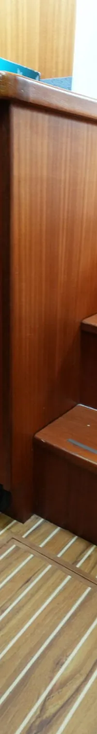 Een interieur van een boot met houten wanden, kasten, vloer en twee treden, en een grijze prullenbak.