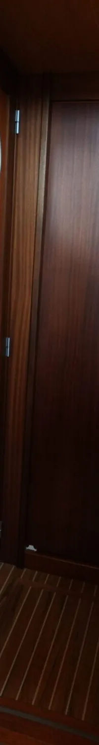 De foto toont een houten interieur van een boot met een blauw-wit geruite kussen, een deur en een trapje.