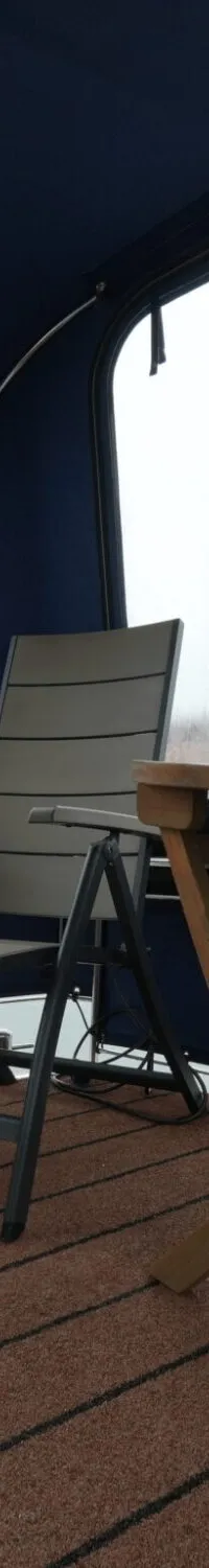 Een interieur van een boot met een bruine vloer, een houten klaptafel en twee stoelen, omringd door ramen.