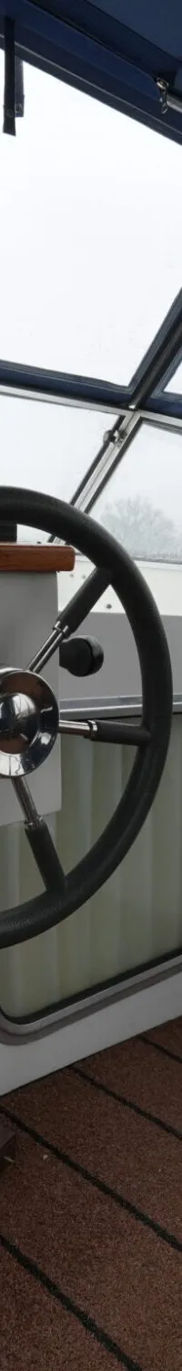 De foto toont een stuurwiel en een deel van de cockpit van een boot, met een ruitenwisser op de voorruit.