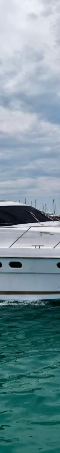 Een witte motorjacht met de naam "Sunshine" vaart op zee onder een bewolkte hemel, met een kustlijn op de achtergrond.