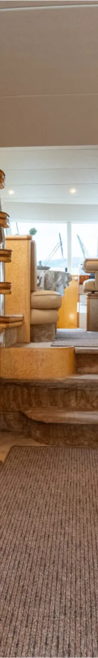 De foto toont een interieur van een boot met een zithoek, een trap, een televisie en houten kasten.
