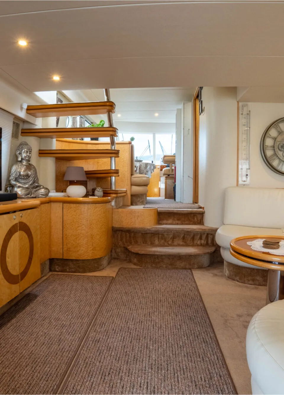 De foto toont een interieur van een boot met een zithoek, een trap, een televisie en houten kasten.