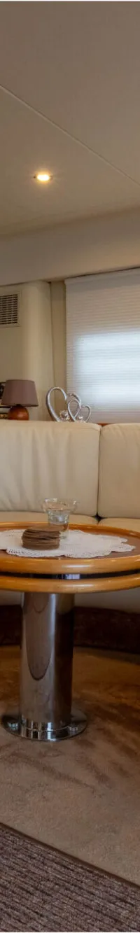 De foto toont een interieur van een boot met een crèmekleurige U-vormige bank, een ronde houten tafel en een tapijt.