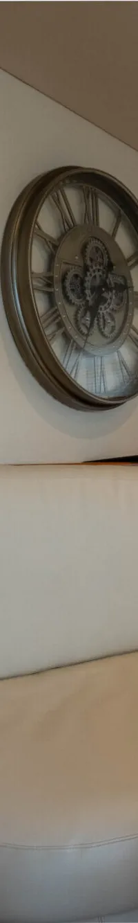 Een interieur van een boot met een beige bank, een klok aan de muur, een trap met bruin tapijt en jaloezieën voor de ramen.