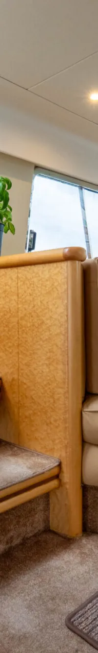 De foto toont het interieur van een boot met een houten trap, een zithoek met tafel en ramen met uitzicht naar buiten.