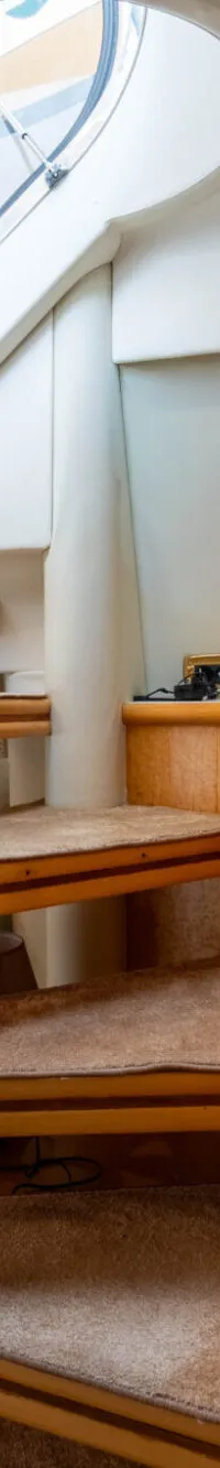 De foto toont het interieur van een boot met een trap, een bank, een televisie en een patrijspoort.