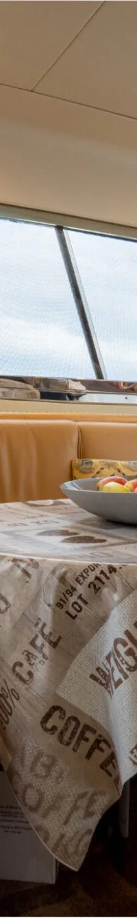 Een interieur van een boot met een U-vormige bank, een tafel met een tafelkleed en een fruitschaal.