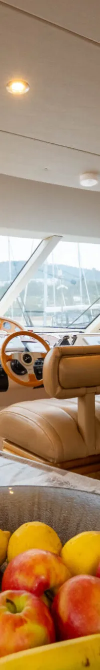 Een interieur van een boot met een tafel met fruit, een vaas met bloemen, een stuurstand en een boekenkast.