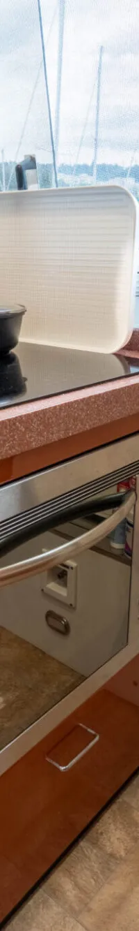 Een kombuis met een kookplaat, oven, gootsteen, kasten en een raam met uitzicht op een haven.