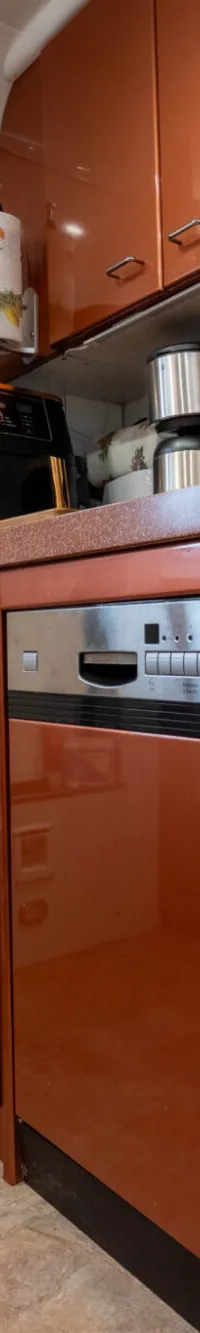 Een kombuis met oranje kasten, een aanrecht met een kraan, een vaatwasser en een deur met patrijspoort.