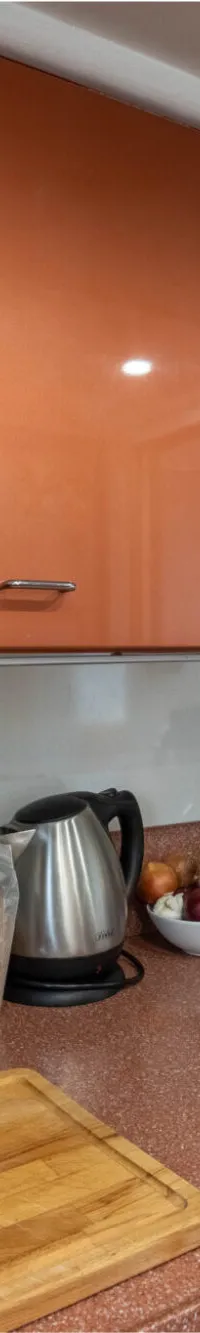 Een keuken met oranje kasten, een aanrecht met spoelbak, een snijplank, en diverse keukenapparatuur en -benodigdheden.