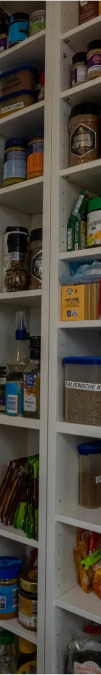 Een interieur van een boot met een stuurstand, een open kast vol met potjes en pakjes, en een kombuis met een…