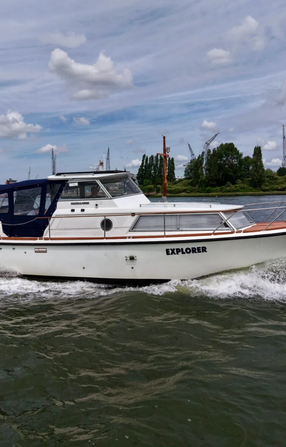 Een witte motorboot met de naam "EXPLORER" vaart op water, met een blauwe kap en registratienummer YD 22-77.