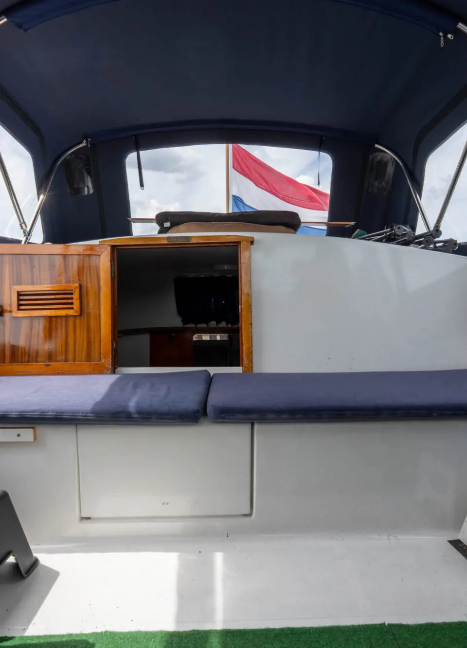 De foto toont het interieur van een boot met een blauwe kap, blauwe kussens en een Nederlandse vlag aan de achterzijde.