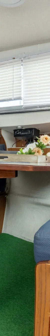 De kajuit toont een zithoek met blauwe kussens, een houten tafel, een tv en drie ronde meters aan de wand.