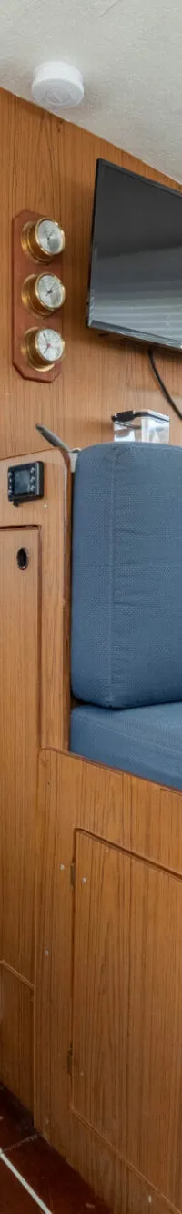 De kajuit van een boot met houten interieur, een blauwe bank, een tafel, een tv en een keukenblokje.